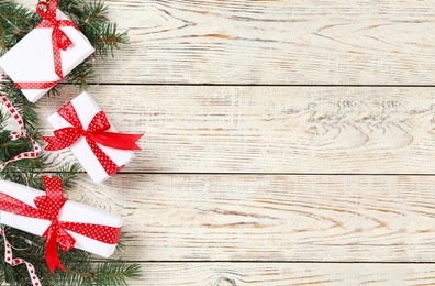 Photo of Christmas gift boxes with red bows and fir branches on white wooden background, flat lay. Space for text