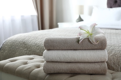 Photo of Stack of fresh towels with flower on soft bench in bedroom. Space for text