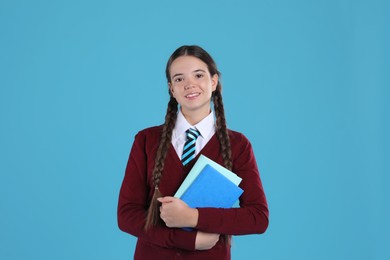 Photo of Teenage girl in school uniform with books on light blue background