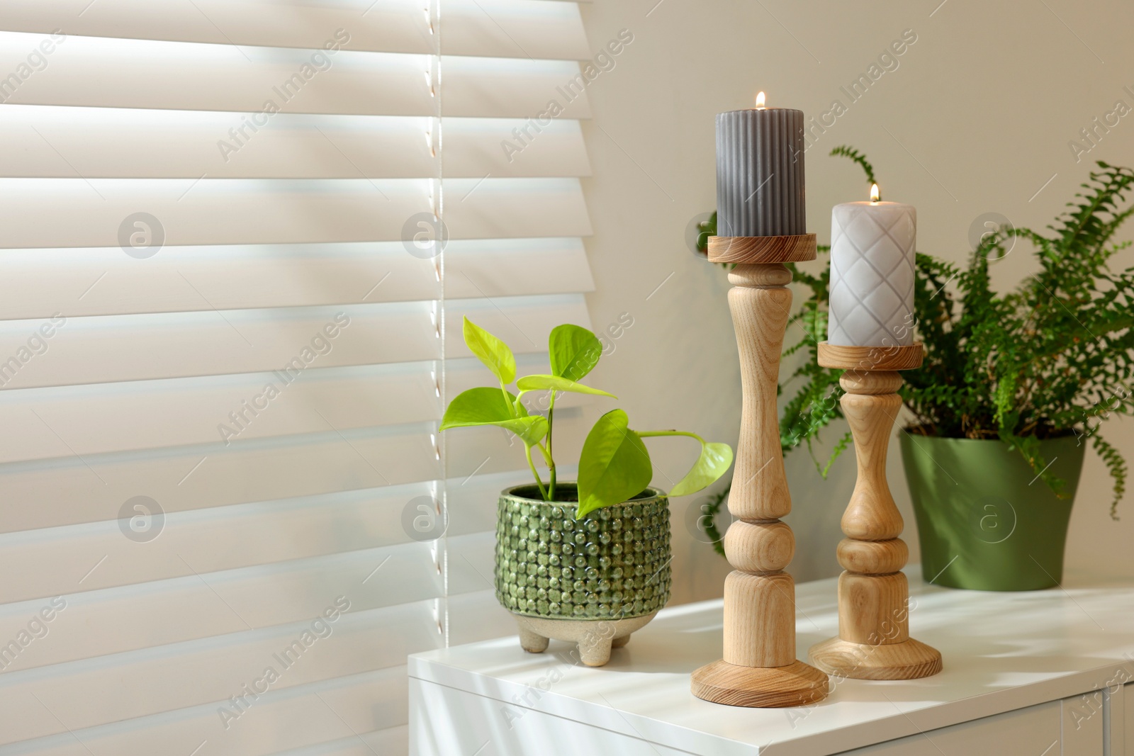 Photo of Pair of beautiful wooden candlesticks and houseplants on white table in room, space for text