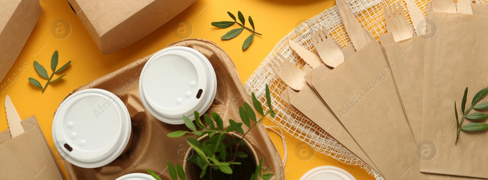 Image of Paper and wooden tableware with green twigs on yellow background, flat lay. Banner design