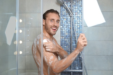 Photo of Attractive young man taking shower with soap in bathroom