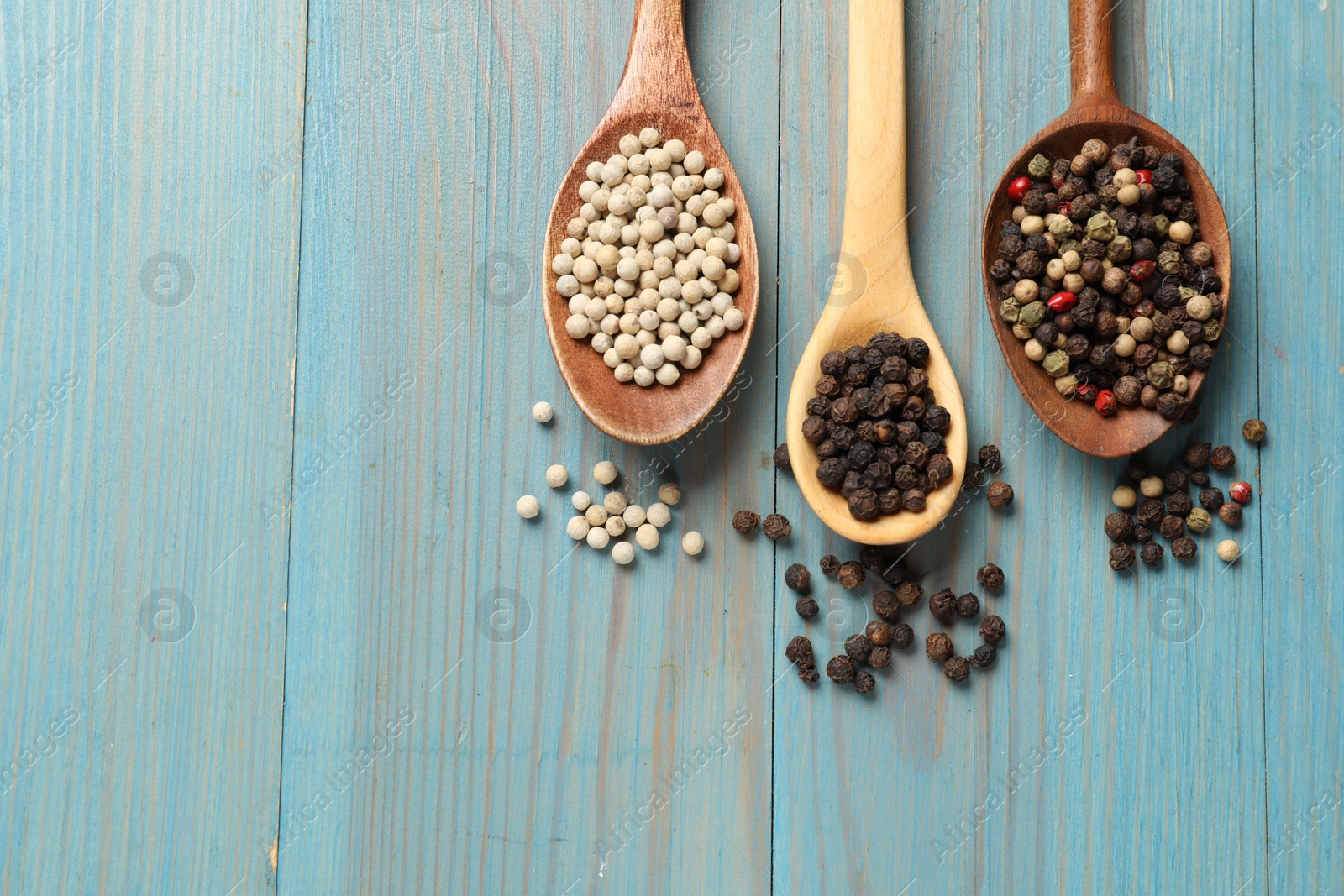 Photo of Aromatic spice. Different peppers in spoons on light blue wooden table, flat lay. Space for text