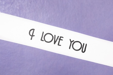 Card with text I Love You on purple leather background, top view