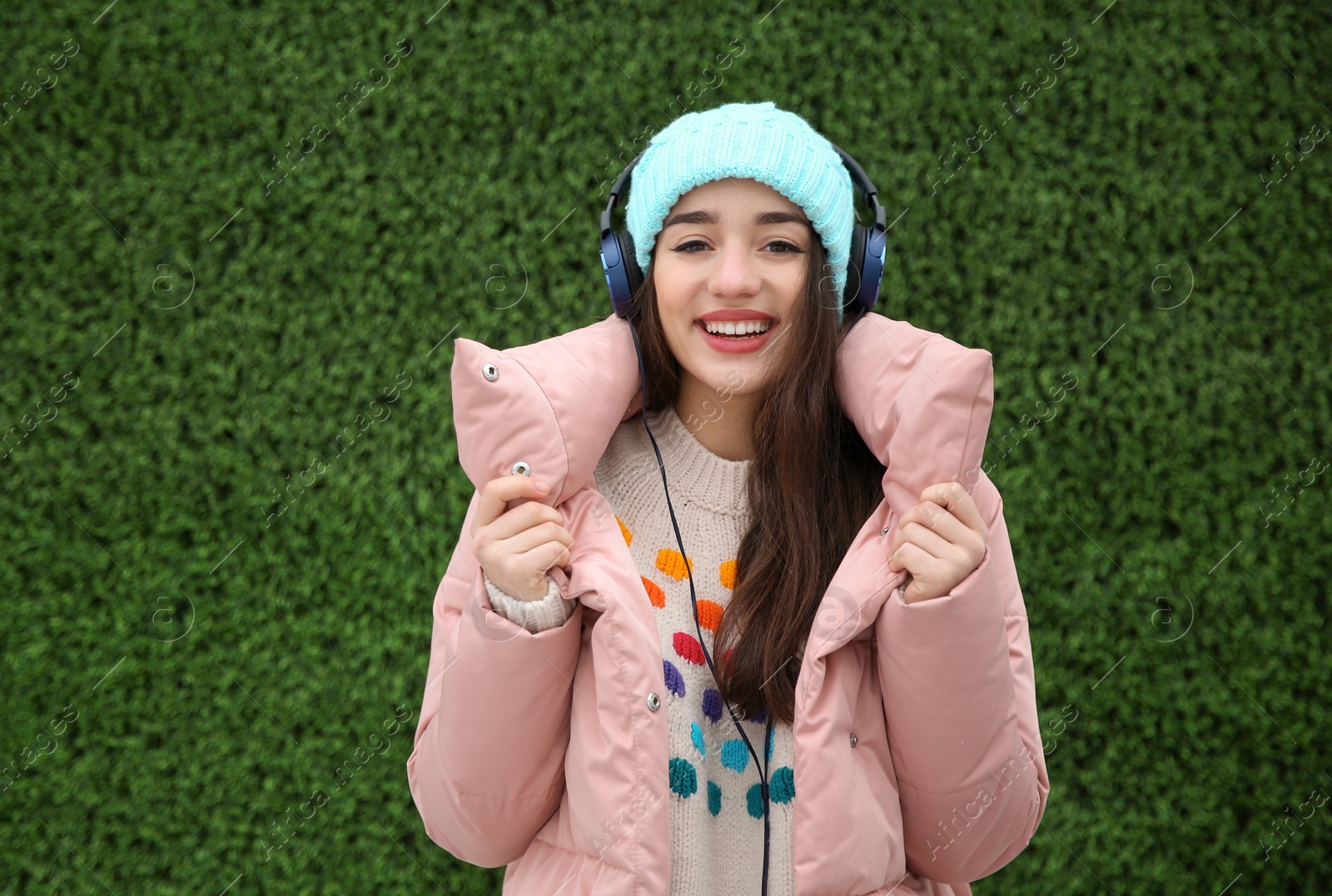 Photo of Beautiful young woman listening to music with headphones near grass wall