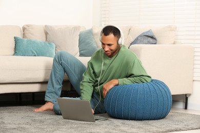 Smiling African American man in headphones with laptop near sofa at home