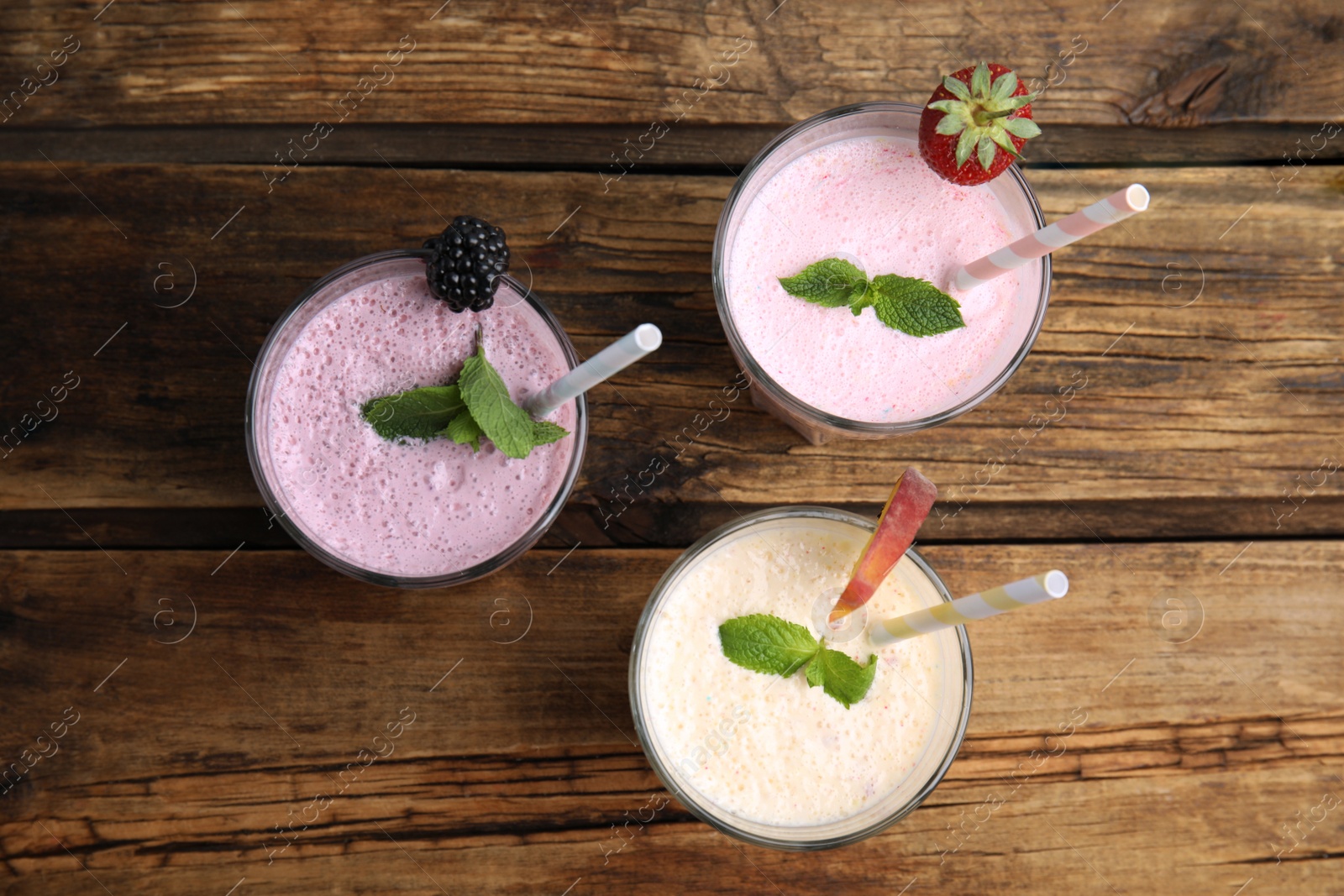 Photo of Different tasty milk shakes on wooden table, flat lay