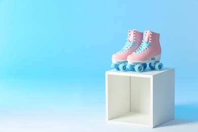 Photo of Pair of vintage roller skates on storage cube against color background. Space for text