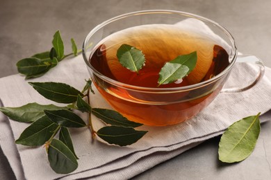 Photo of Cup of freshly brewed tea with bay leaves on grey table, closeup