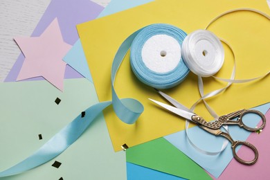 Pair of scissors with ribbons and colorful paper sheets on white wooden table, flat lay