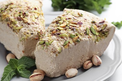 Photo of Pieces of tasty halva with pistachios and mint on plate, closeup