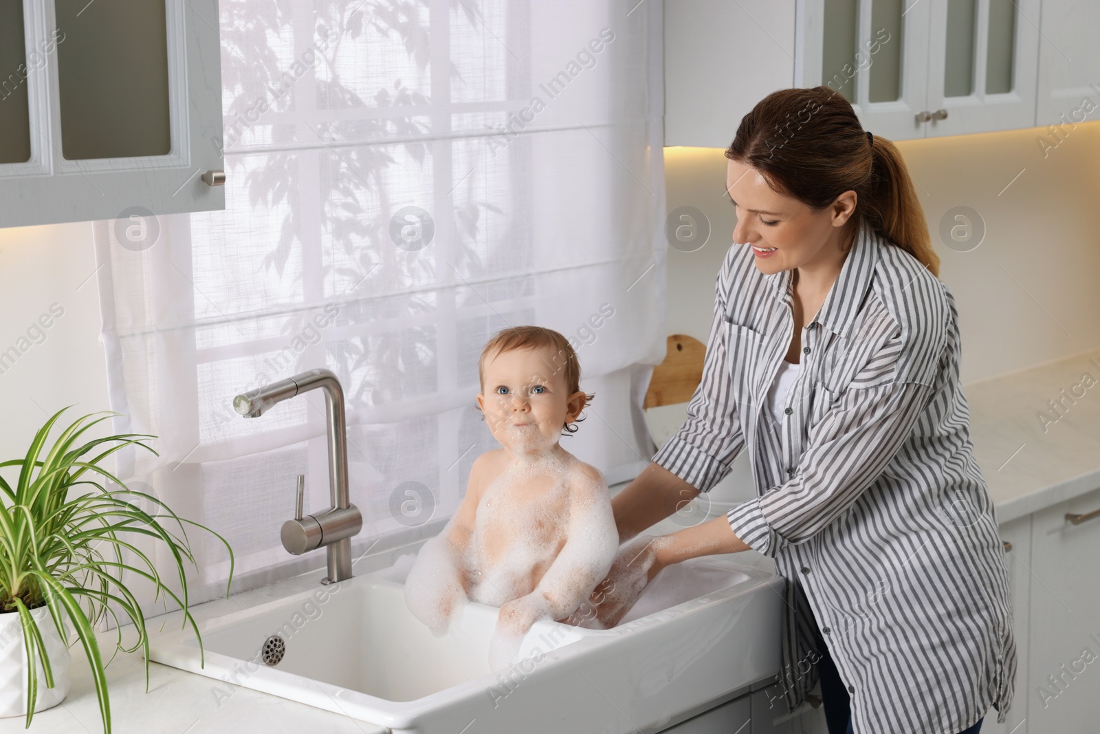 Photo of Mother washing her little baby in sink at home