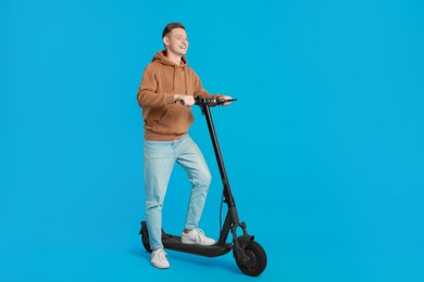 Happy man with modern electric kick scooter on light blue background