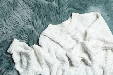 Photo of White knitted sweater on green fur rug, flat lay