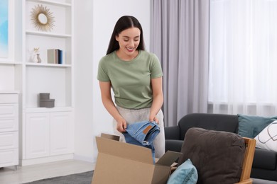Happy young woman taking jeans out of box at home. Online shopping