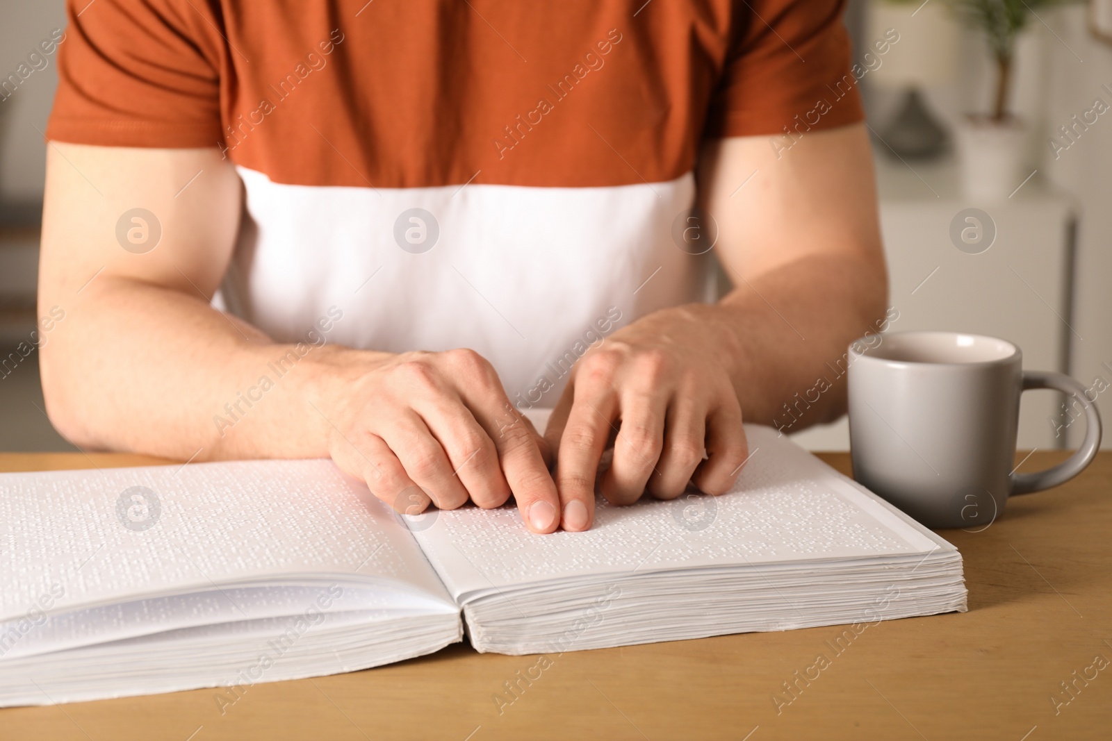 Photo of Blind man reading book written in Braille at table, closeup