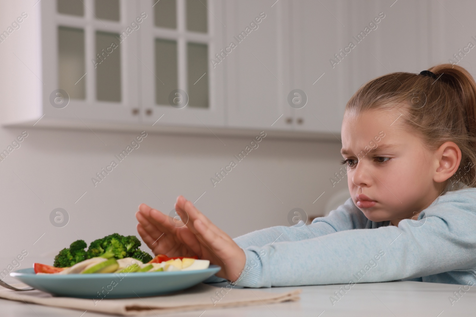 Photo of Cute little girl refusing to eat dinner in kitchen, space for text