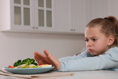 Cute little girl refusing to eat dinner in kitchen, space for text