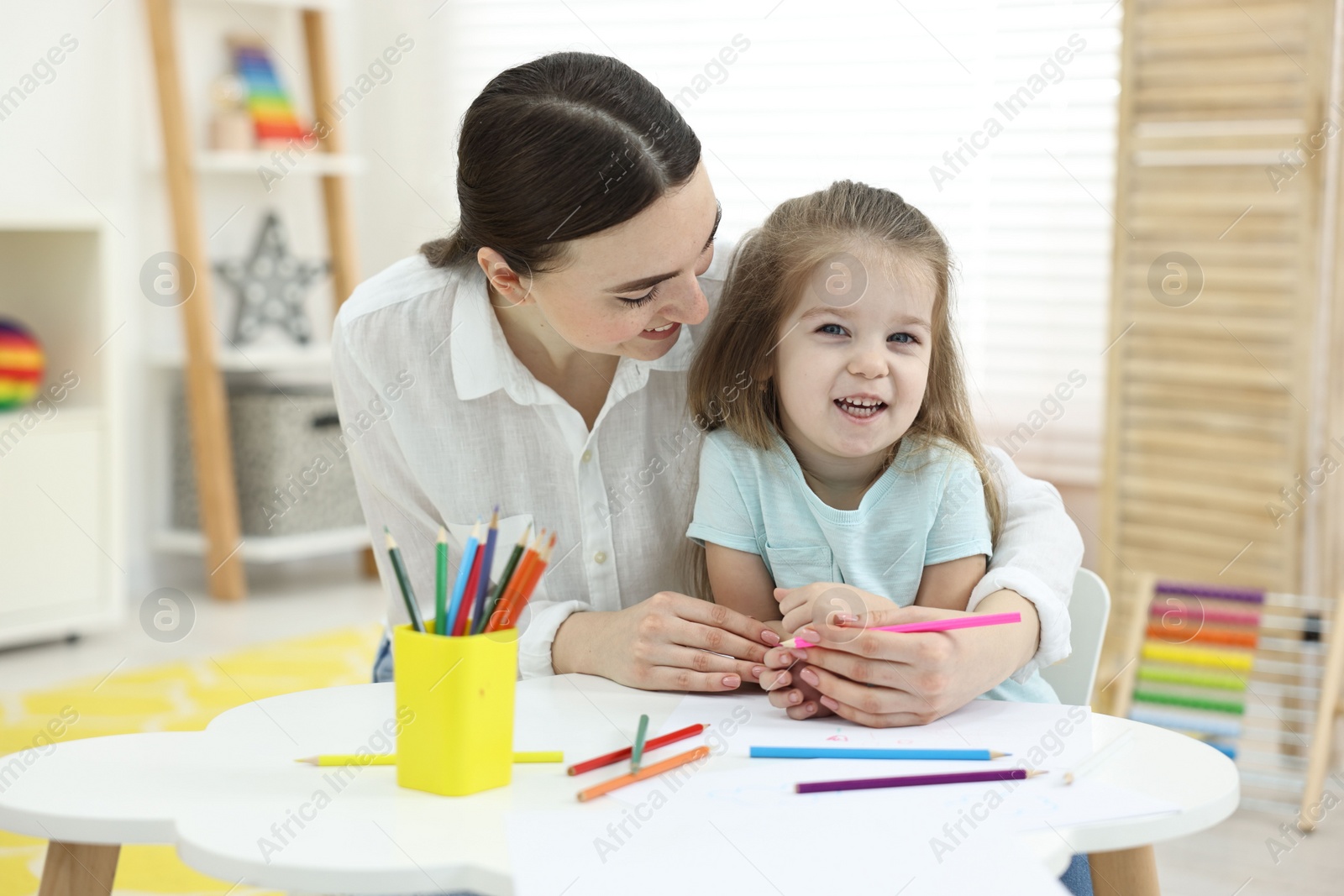 Photo of Mother and her little daughter drawing with colorful pencils at home