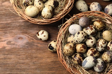 Wicker bowls, quail eggs and straw on wooden table, flat lay. Space for text