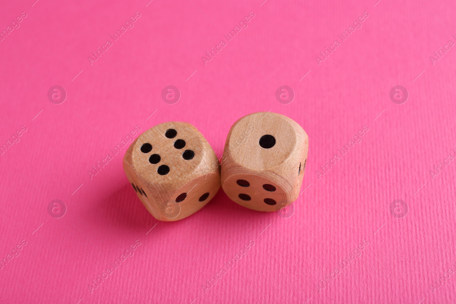 Photo of Two wooden game dices on pink background, closeup