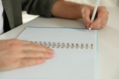Photo of Left-handed man writing in notebook at white table, closeup
