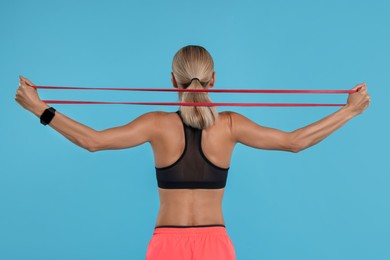 Woman exercising with elastic resistance band on light blue background, back view