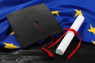Photo of Graduation cap, diploma and flag of European Union on black wooden table