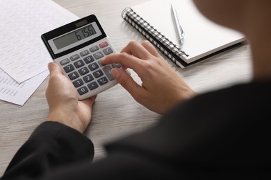 Photo of Woman using calculator at light wooden table, closeup
