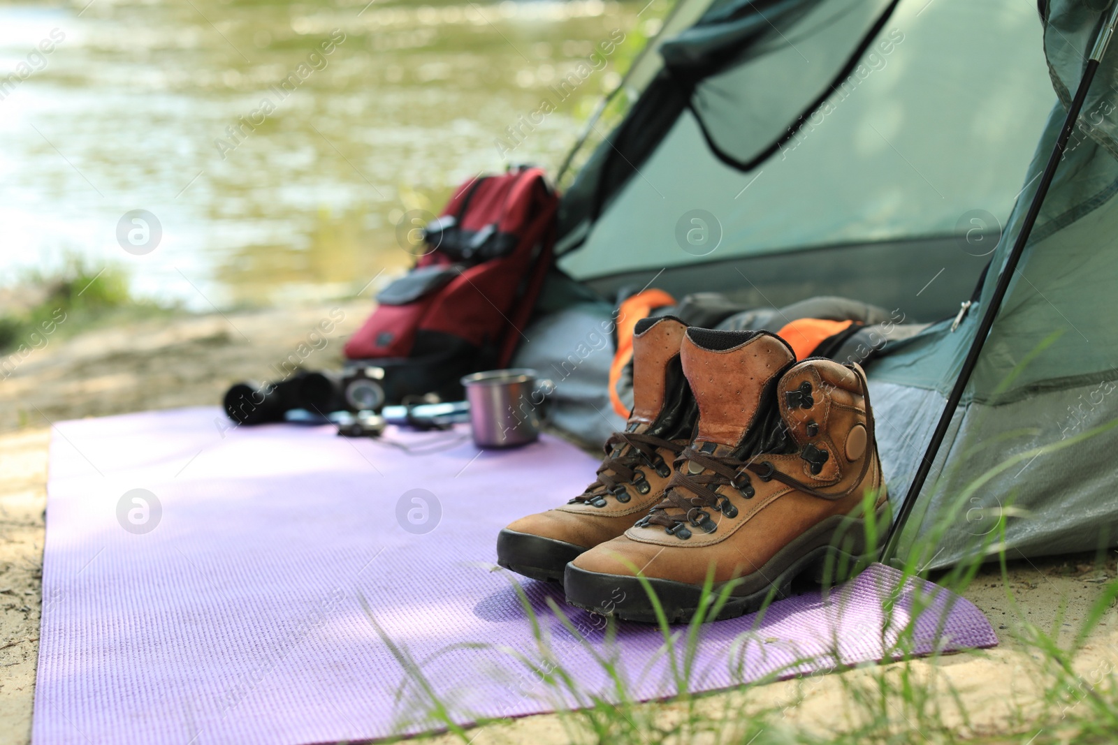 Photo of Boots and camping equipment near tent on riverbank. Space for text