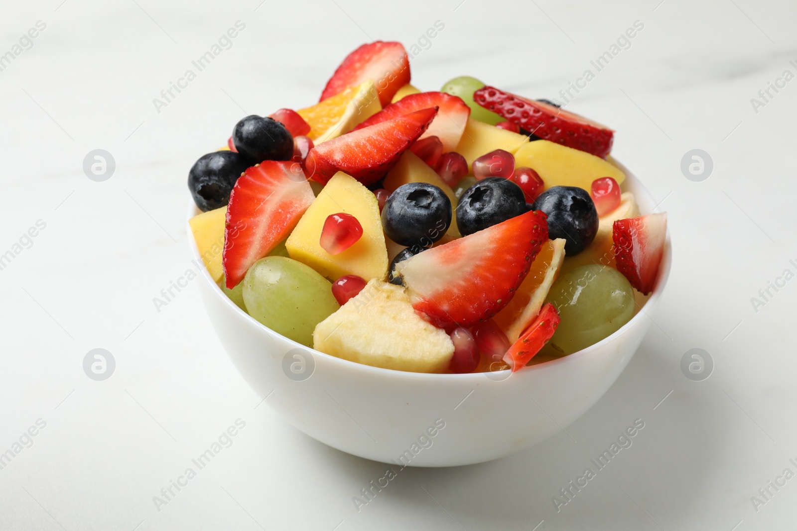 Photo of Tasty fruit salad in bowl on white table, closeup