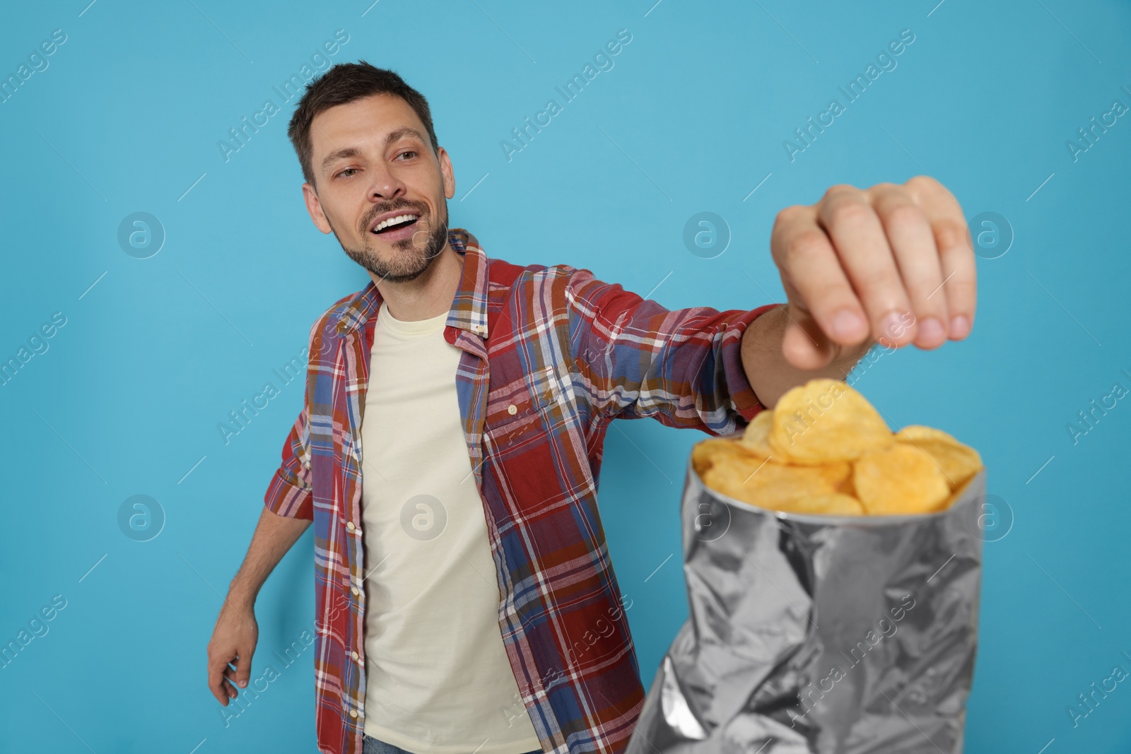 Photo of Handsome man eating potato chips on light blue background