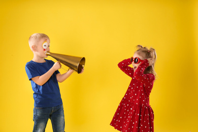 Photo of Funny kids with megaphone on yellow background. April fool's day