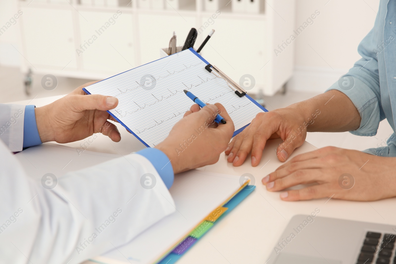 Photo of Male doctor showing cardiogram to patient in clinic. Cardiology consultation