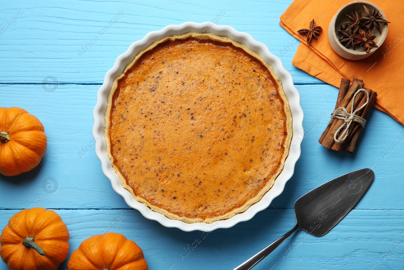 Photo of Delicious pumpkin pie and ingredients on light blue wooden table, flat lay