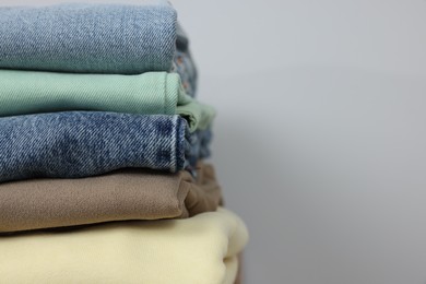 Photo of Stack of different folded clothes near grey wall, closeup. Space for text