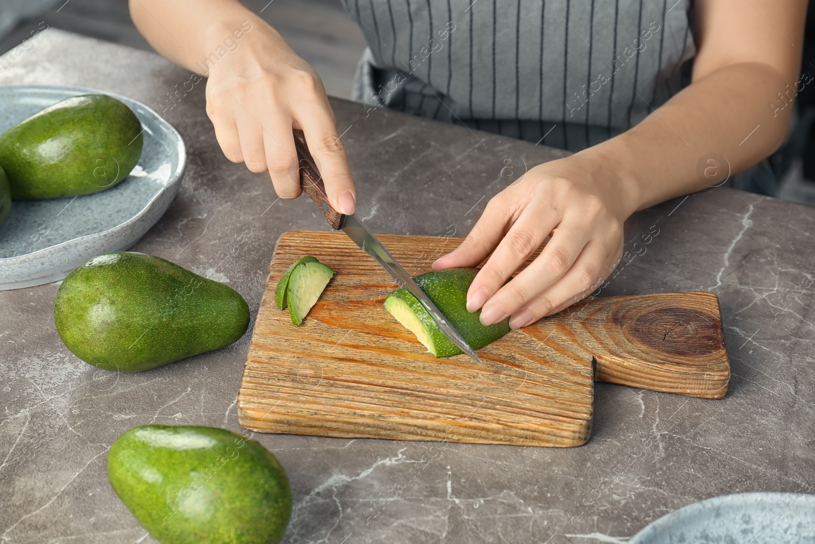 Photo of Woman cutting ripe avocado on wooden board at table