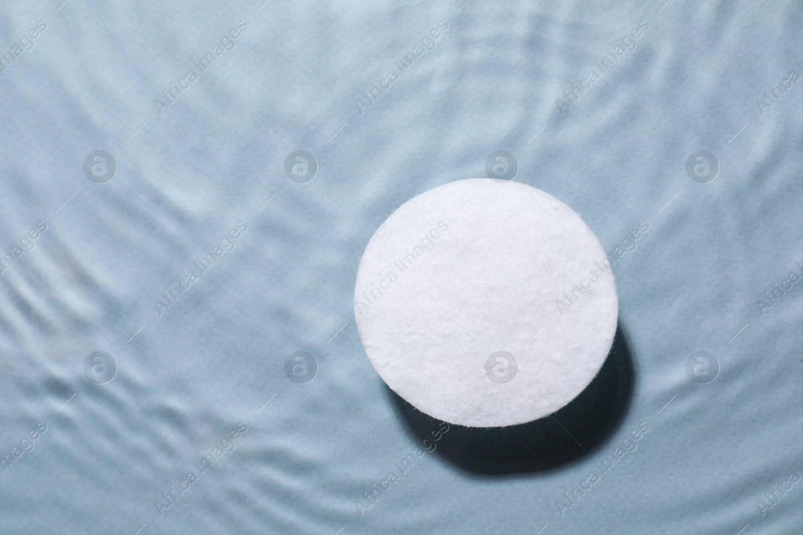 Photo of Cotton pad in micellar water on light grey background, top view. Space for text