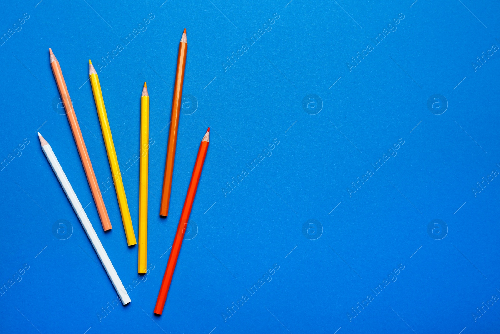 Photo of Color pencils on blue background, flat lay. Space for text