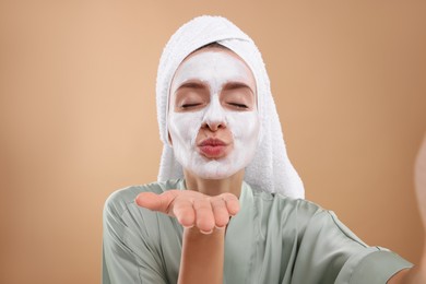 Photo of Woman with face mask blowing kiss while taking selfie on beige background. Spa treatments