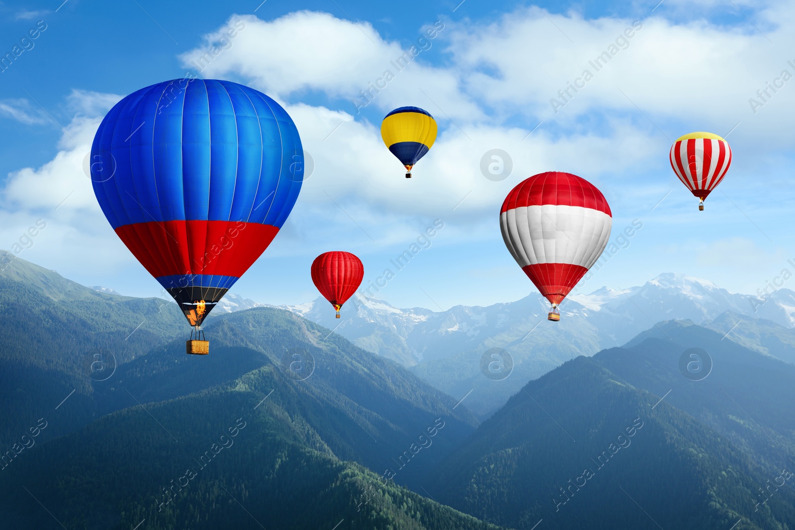 Image of Bright hot air balloons flying in sky with clouds over mountains