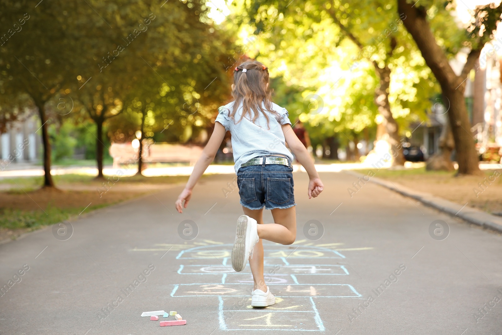 Photo of Little child playing hopscotch drawn with colorful chalk on asphalt