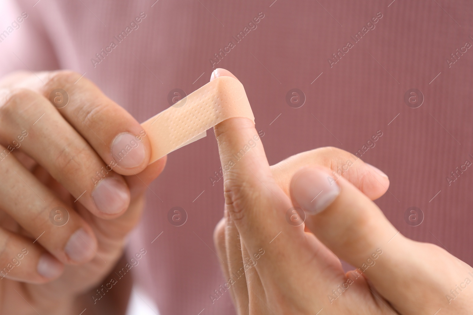 Photo of Man applying adhesive bandage on finger, closeup view