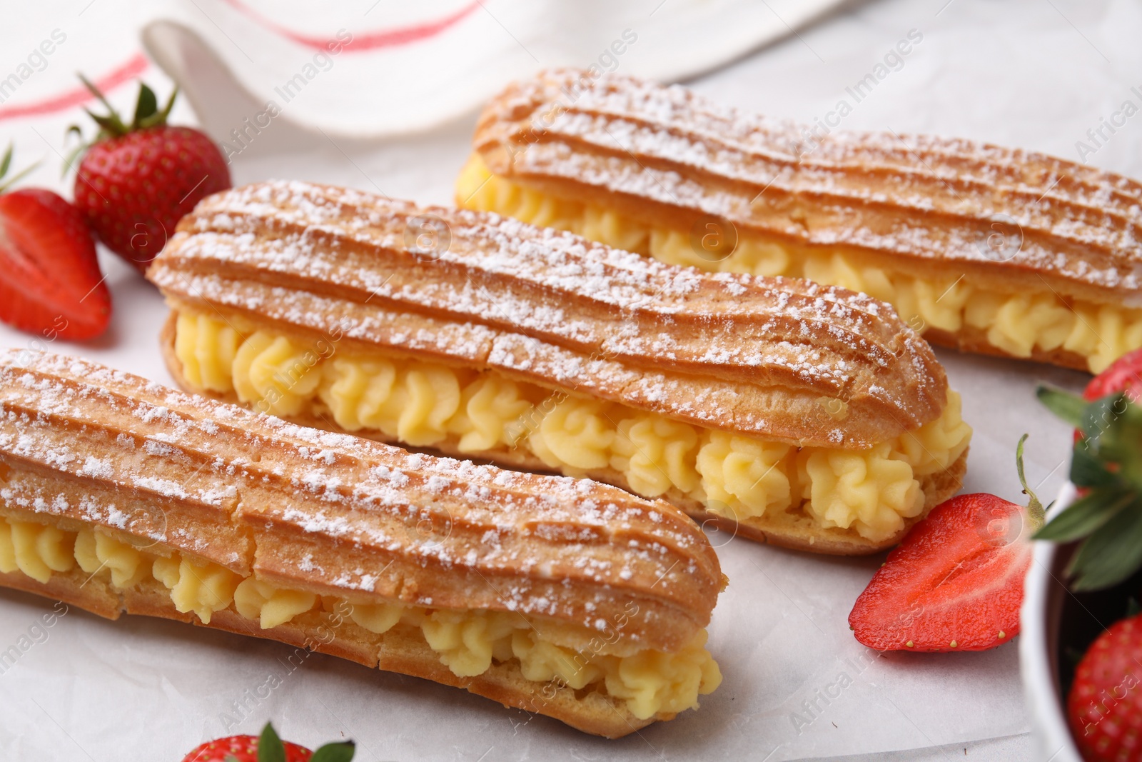 Photo of Delicious eclairs filled with cream and strawberries on table, closeup