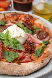 Photo of Delicious pizza with burrata cheese, basil, ham and sun-dried tomatoes on table, closeup
