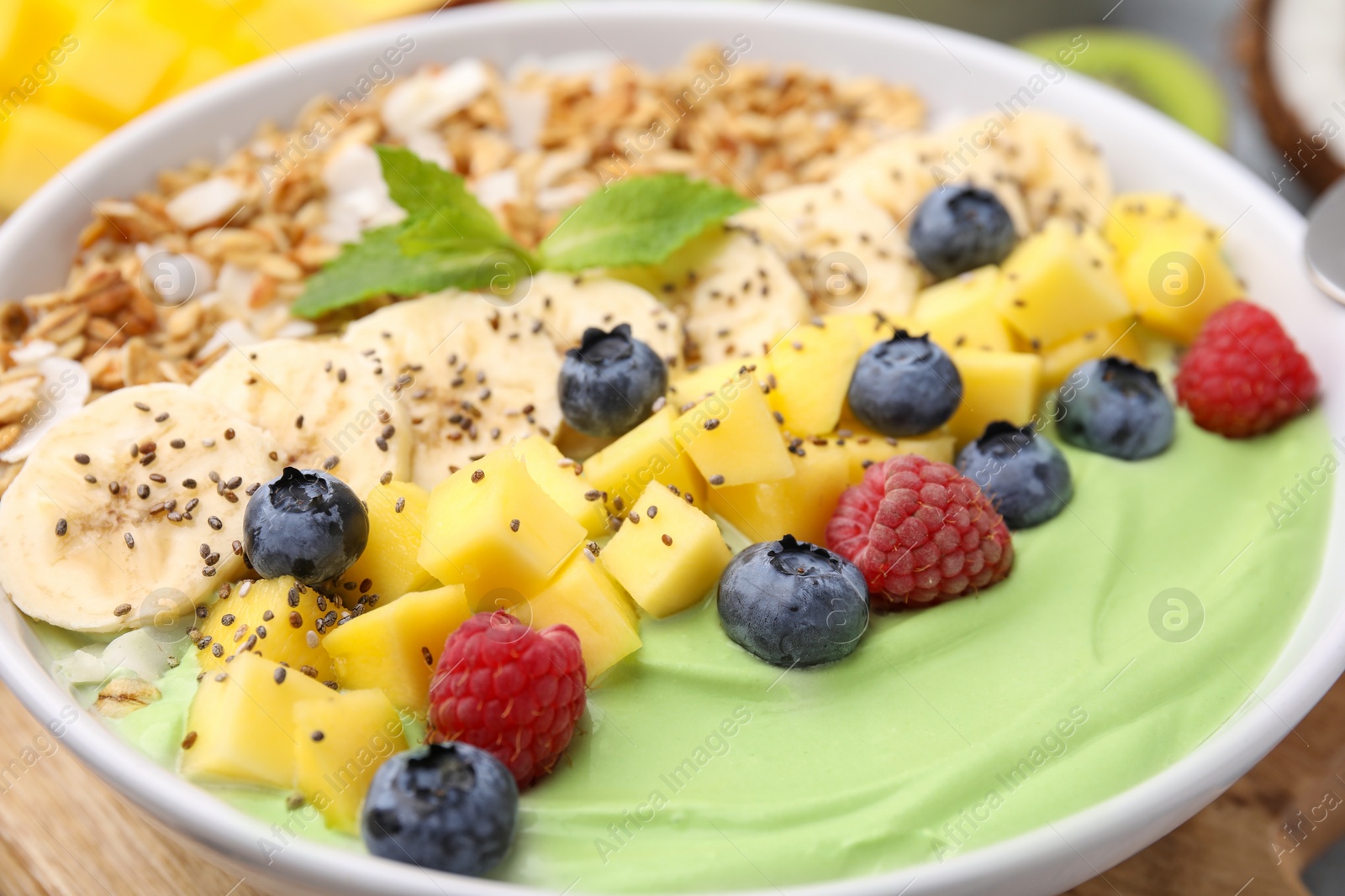 Photo of Tasty matcha smoothie bowl served with fresh fruits and oatmeal on table, closeup. Healthy breakfast