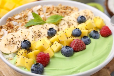 Tasty matcha smoothie bowl served with fresh fruits and oatmeal on table, closeup. Healthy breakfast
