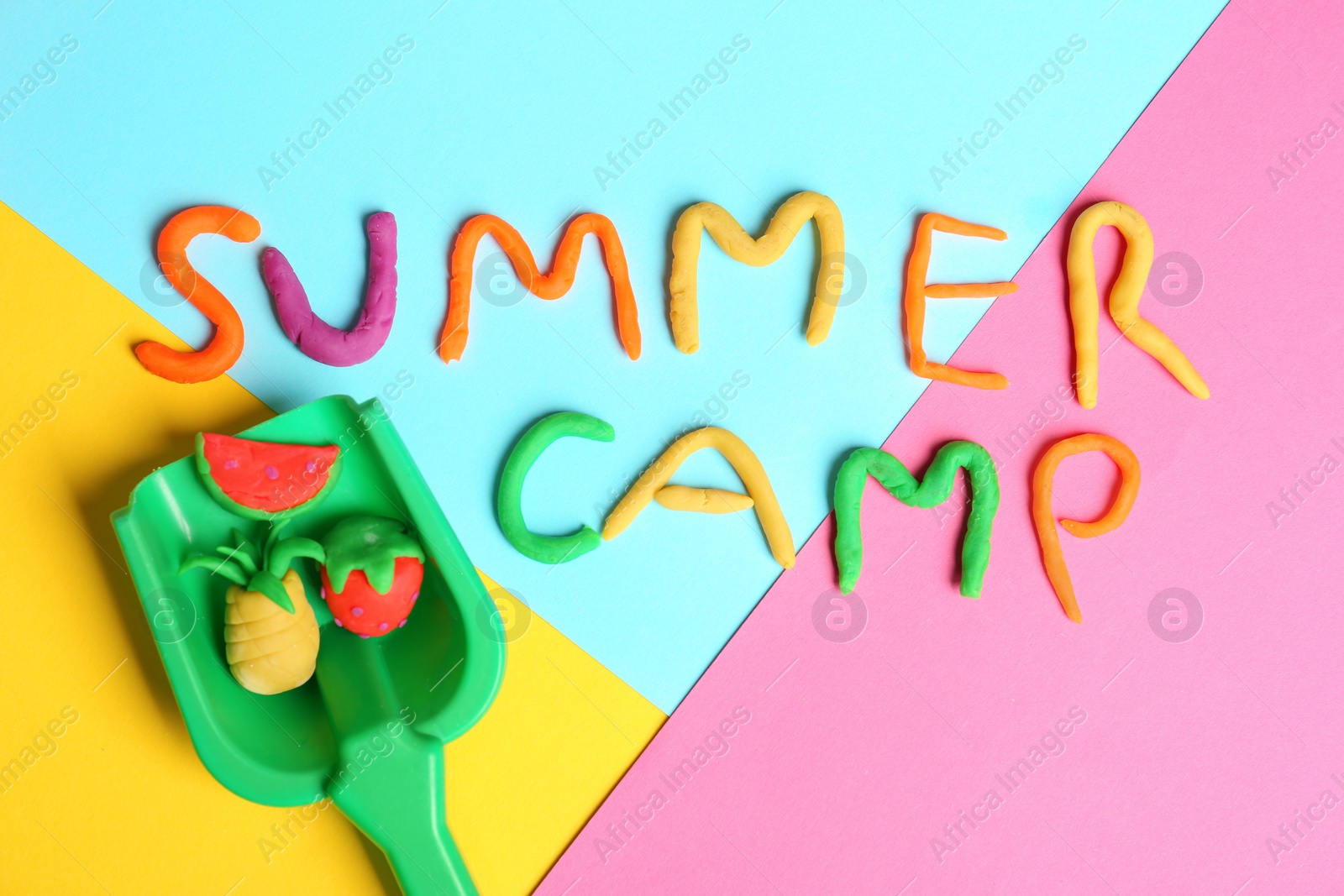 Photo of Flat lay composition with words SUMMER CAMP made from modelling clay and plastic shovel on color background