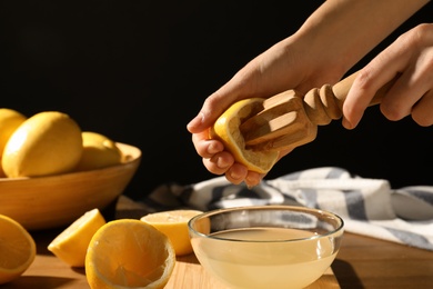 Photo of Woman squeezing lemon juice with wooden reamer into glass bowl at table