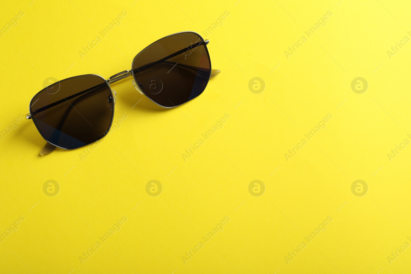 Photo of Stylish sunglasses on yellow background, top view. Space for text